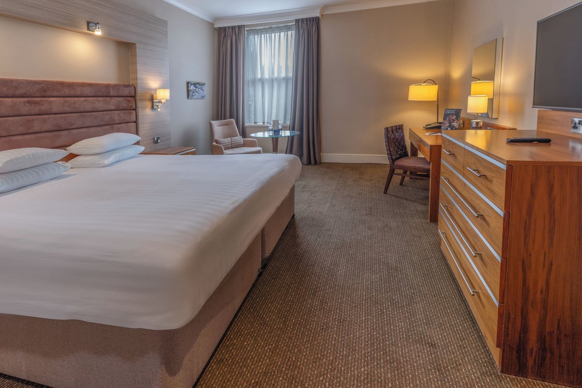 A hotel room with a large bed, a wooden dresser, a desk, and a chair.