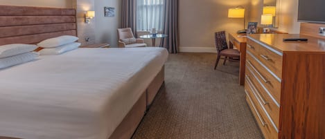 A hotel room with a large bed, a wooden dresser, a desk, and a chair.