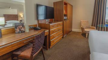 A hotel room with a wooden desk, a television, a minibar, a sofa, and a large mirror.