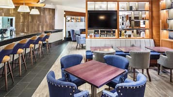 A modern restaurant with bar seating, a large flat-screen TV, and a variety of chairs and tables.