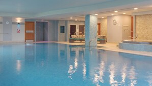 A large indoor swimming pool with a tiled wall, a bench, and a small jacuzzi area.