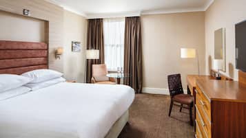 Habitación de hotel con una cama grande, un escritorio, una silla, un televisor y una ventana con cortinas.