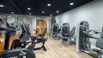 A gym with various exercise machines, wooden flooring, and mirrored walls.