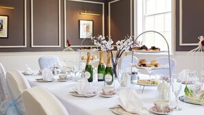 A dining area with a table set for a meal, including plates, glasses, and a cake stand. - Macdonald New Blossoms Hotel, Chester (Chester)
