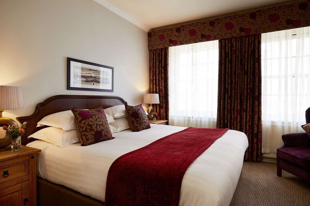 A hotel room with a large bed, two bedside tables, a framed picture on the wall, and a window with curtains.