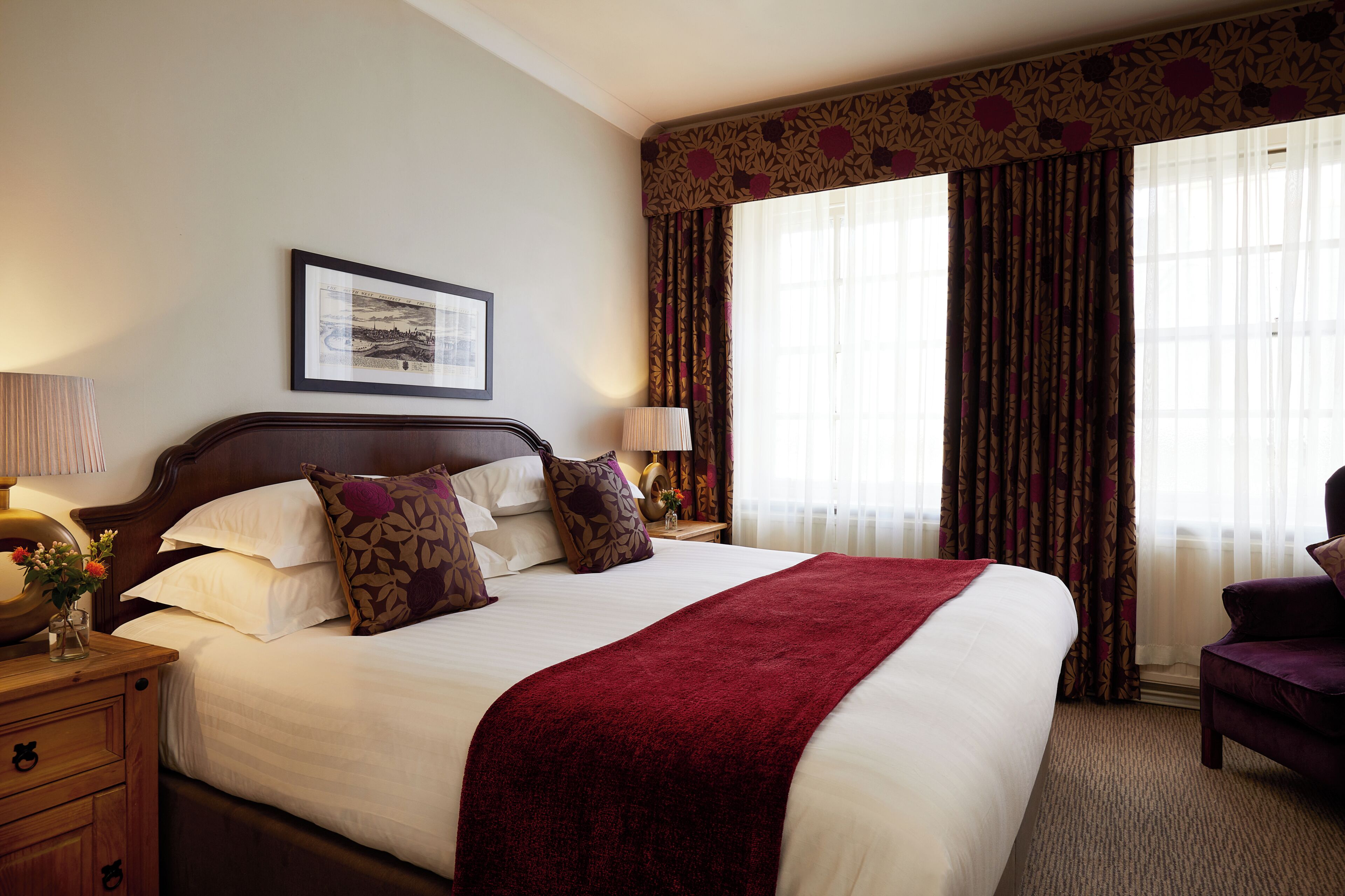 A hotel room with a large bed, two bedside tables with lamps, a framed picture on the wall, and a window with curtains.