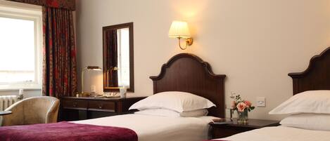 A hotel room with two beds, a nightstand, a lamp, a chair, and a window with curtains.