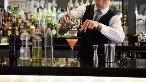A bartender preparing a drink at a bar with various bottles and glasses. - Macdonald New Blossoms Hotel, Chester (Chester)