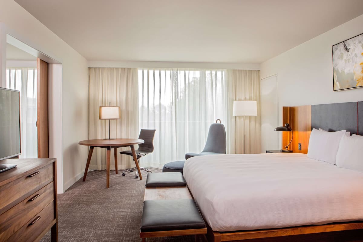 A hotel room with a large bed, a desk with a chair, a TV, and a window with curtains.