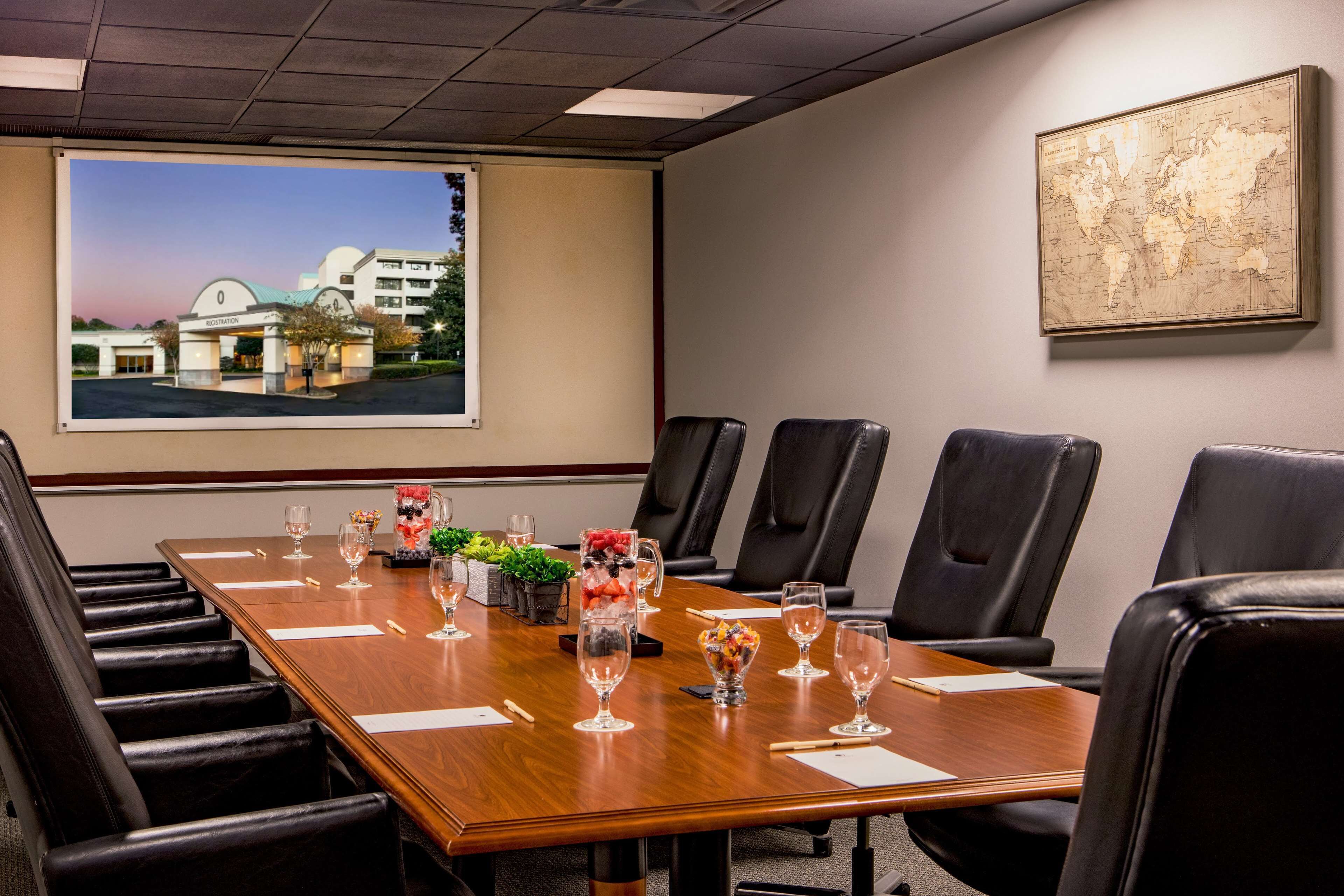 A conference room with a large table, black leather chairs, and a large window with a view of a hotel building.