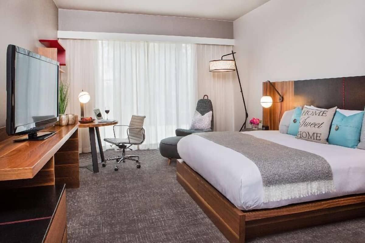 A hotel room with a bed, desk, chair, TV, and a window with curtains.
