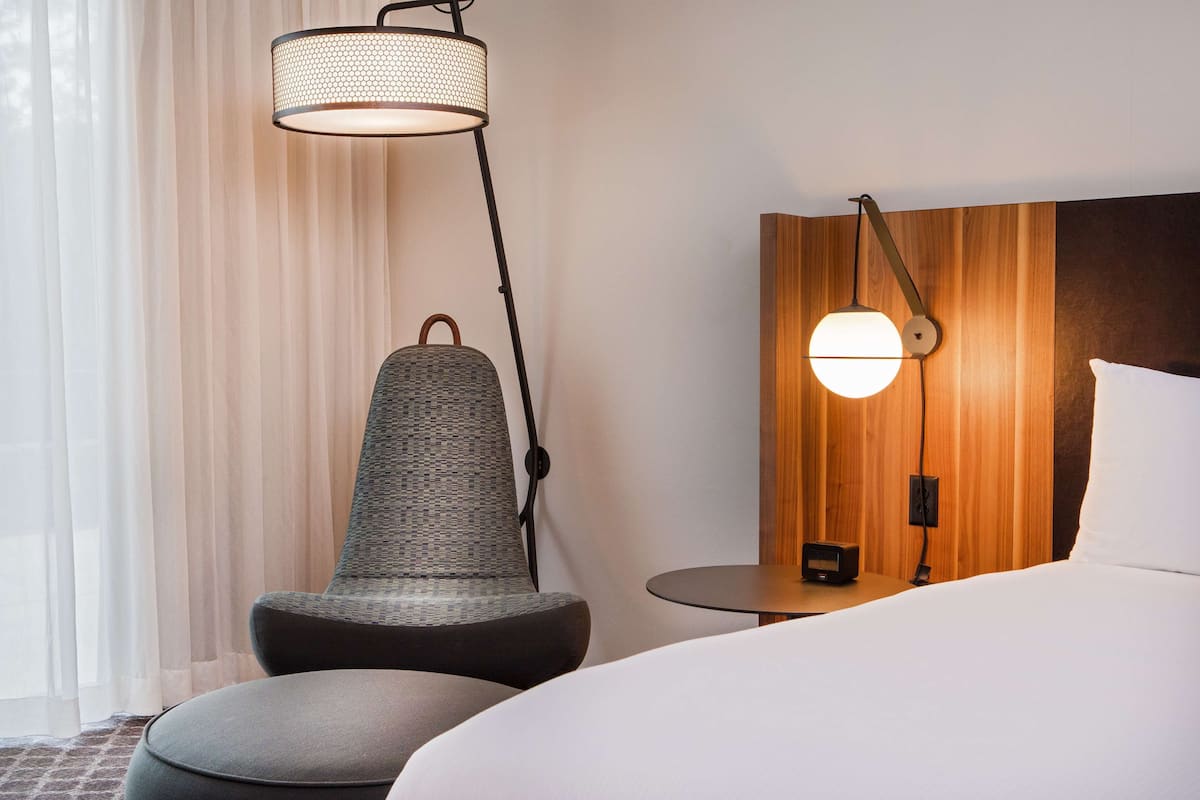 A hotel room with a bed, a round table, a chair, and a floor lamp.