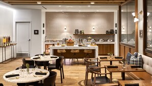 A modern dining area with round tables, bar stools, and a central island with a kitchen in the background. - DoubleTree by Hilton Atlanta Windy Hill Ballpark (Atlanta)