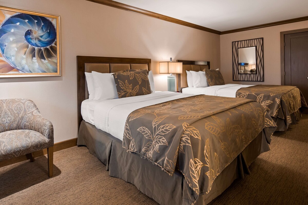 Een hotelkamer met twee bedden, een stoel, een schilderij en een spiegel.