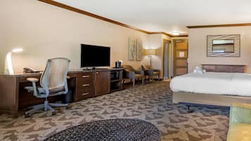 A hotel room with a bed, a desk with a TV, a chair, a lamp, and a patterned carpet.