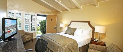 A hotel room with a bed, two bedside lamps, a desk with a computer monitor, a chair, and a ceiling fan.