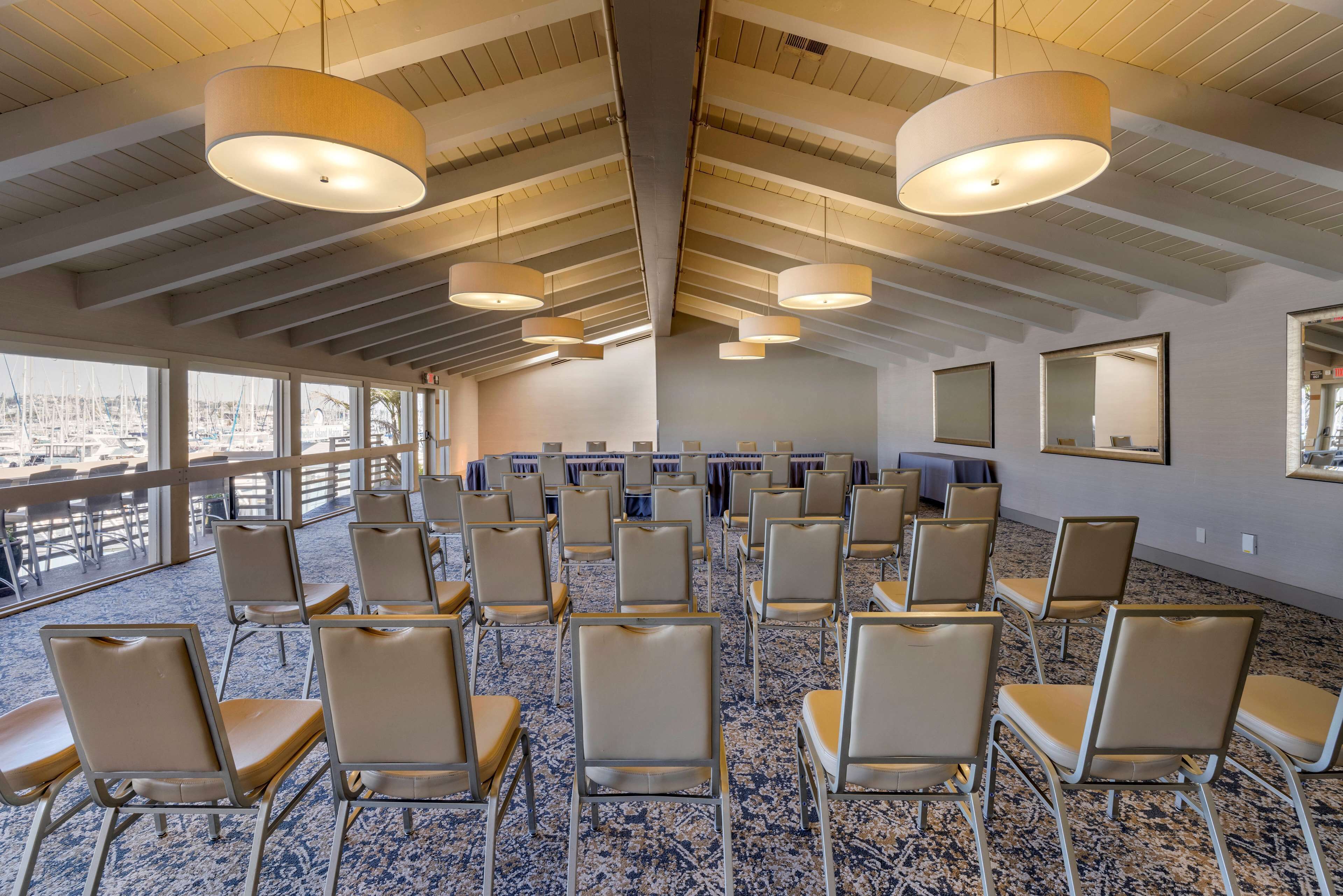 A conference room with rows of chairs, large windows, and a high ceiling with exposed beams.
