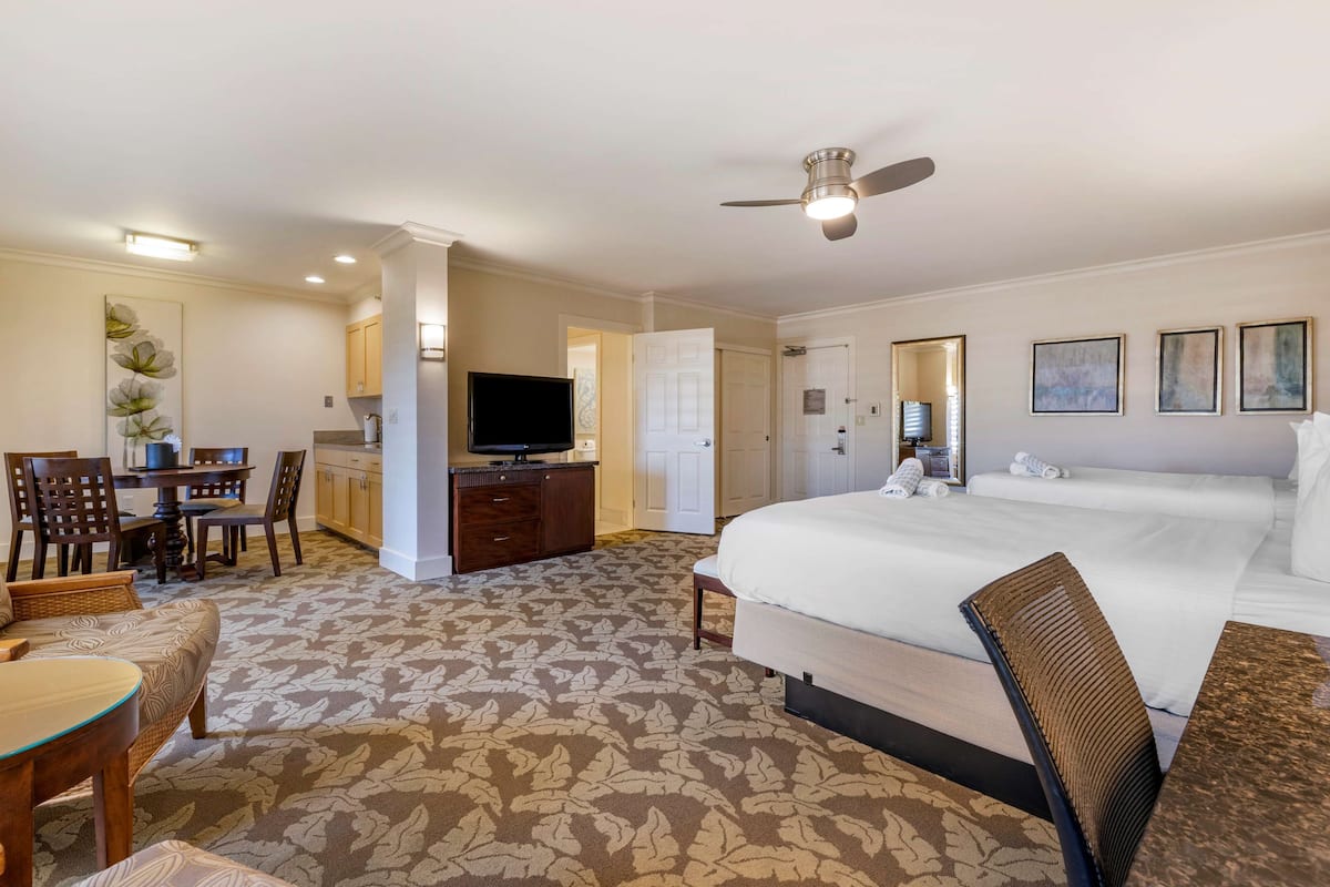 Une chambre d’hôtel dotée d’un grand lit, d’un bureau avec une télévision, d’un coin repas avec des chaises et d’un sol recouvert de moquette.