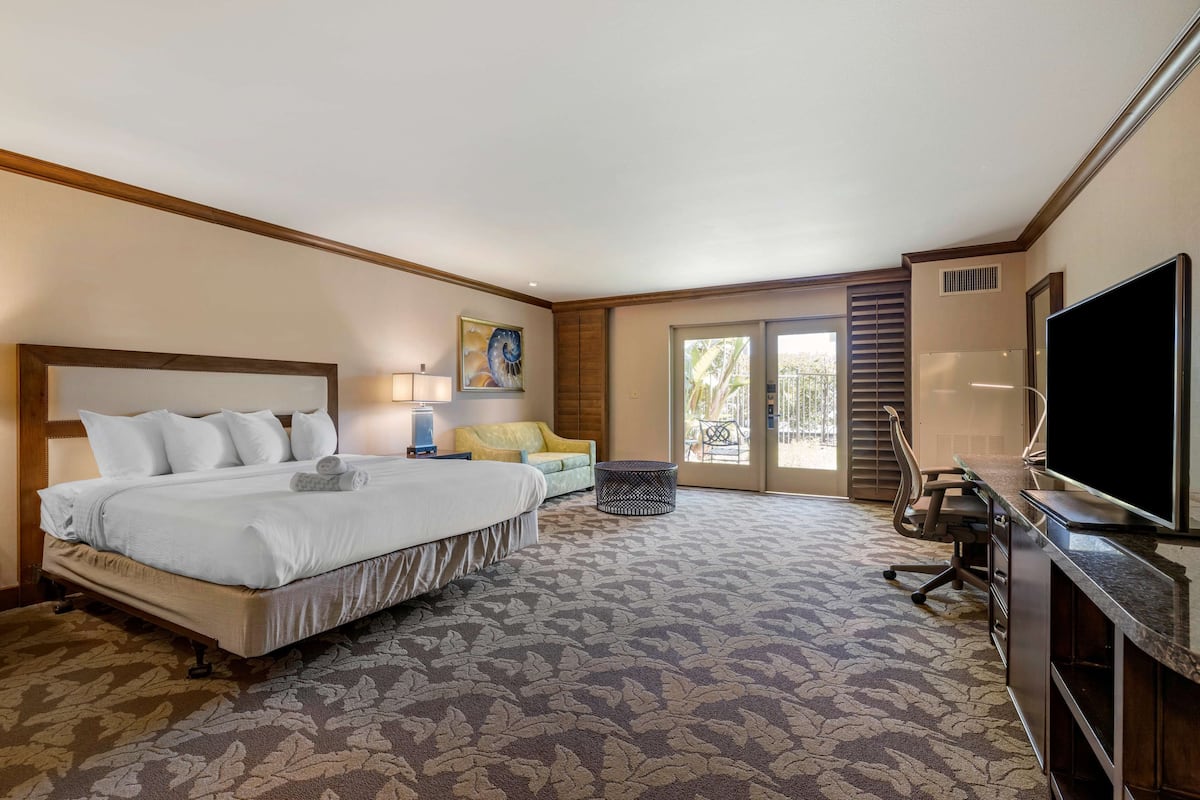 Une chambre d’hôtel avec un grand lit, un bureau doté d’un téléviseur à écran plat, une chaise, une lampe et une fenêtre avec des stores.