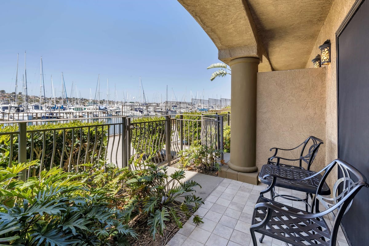 Un balcon donnant sur une marina, un banc en métal et des plantes en pot.