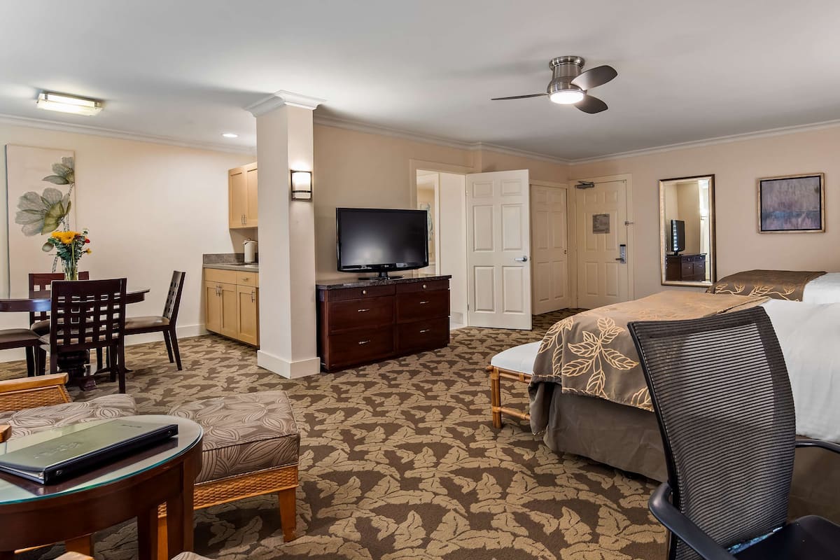 Une chambre d’hôtel comprenant un lit, un bureau avec un ordinateur, une télévision et un coin repas avec des chaises et une table.