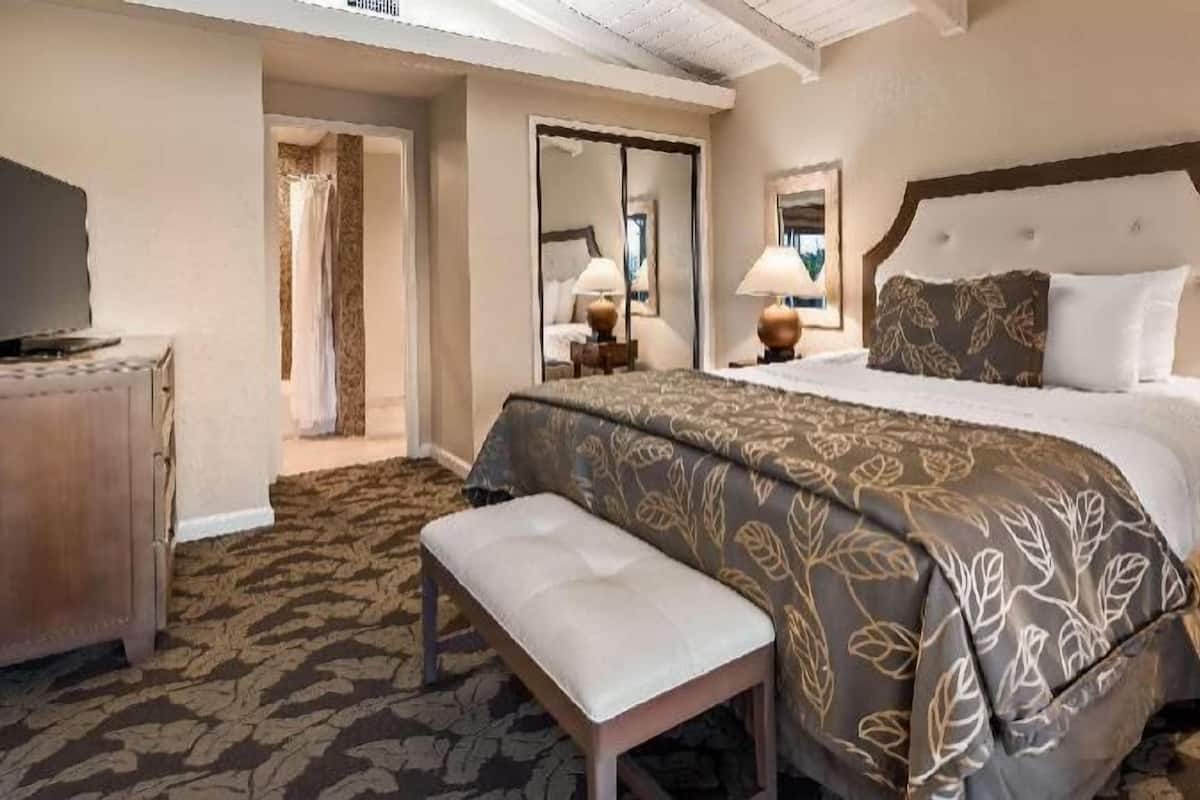 Une chambre d’hôtel avec un grand lit, un banc, un bureau et un miroir.