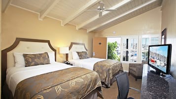 A hotel room with two beds, a desk with a TV, and a view of the marina through the window.