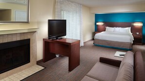 A hotel room with a television on a wooden desk, a bed with a blue headboard, a sofa, and a fireplace. - Residence Inn by Marriott Nashville Airport (Nashville)