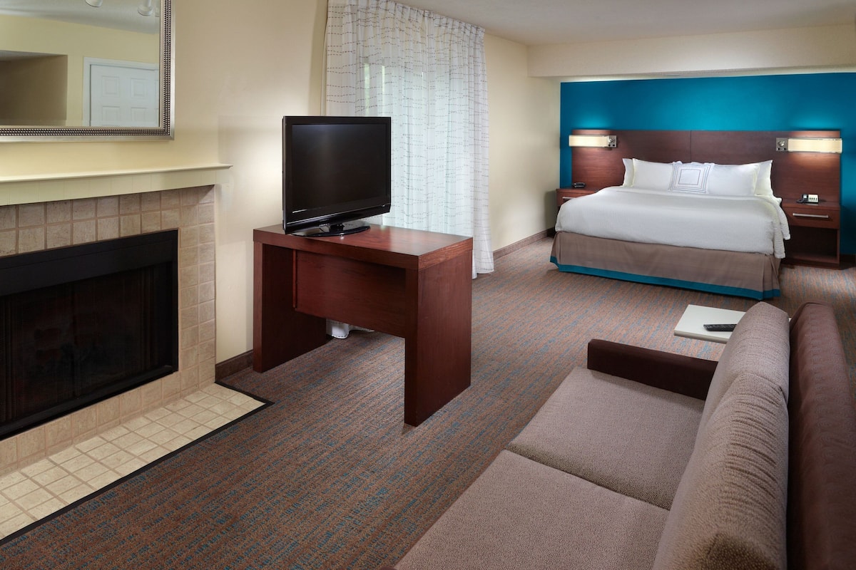 A hotel room with a television on a wooden desk, a bed with a blue headboard, a sofa, and a fireplace.