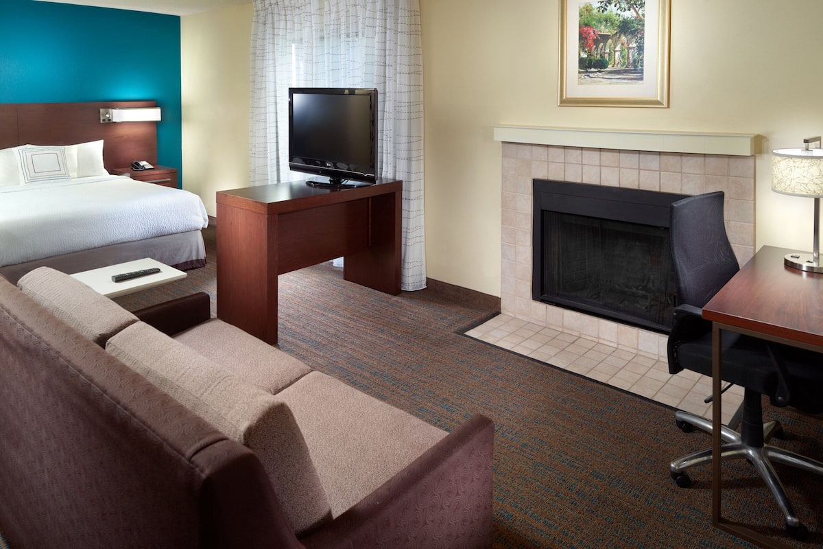 A hotel room with a bed, a TV on a wooden table, a fireplace, a sofa, and a desk.