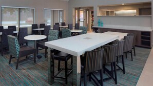 A hotel lobby with multiple seating areas, including round tables and bar stools, carpeted flooring, and a kitchen area with a counter and stools. - Residence Inn by Marriott Nashville Airport (Nashville)