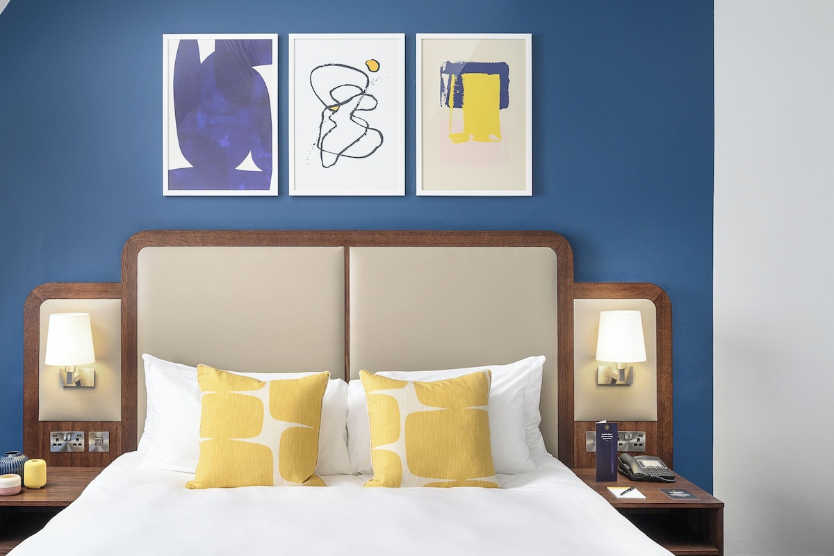Habitación de hotel con una cama grande, dos mesitas de noche y tres obras de arte colgadas en la pared.