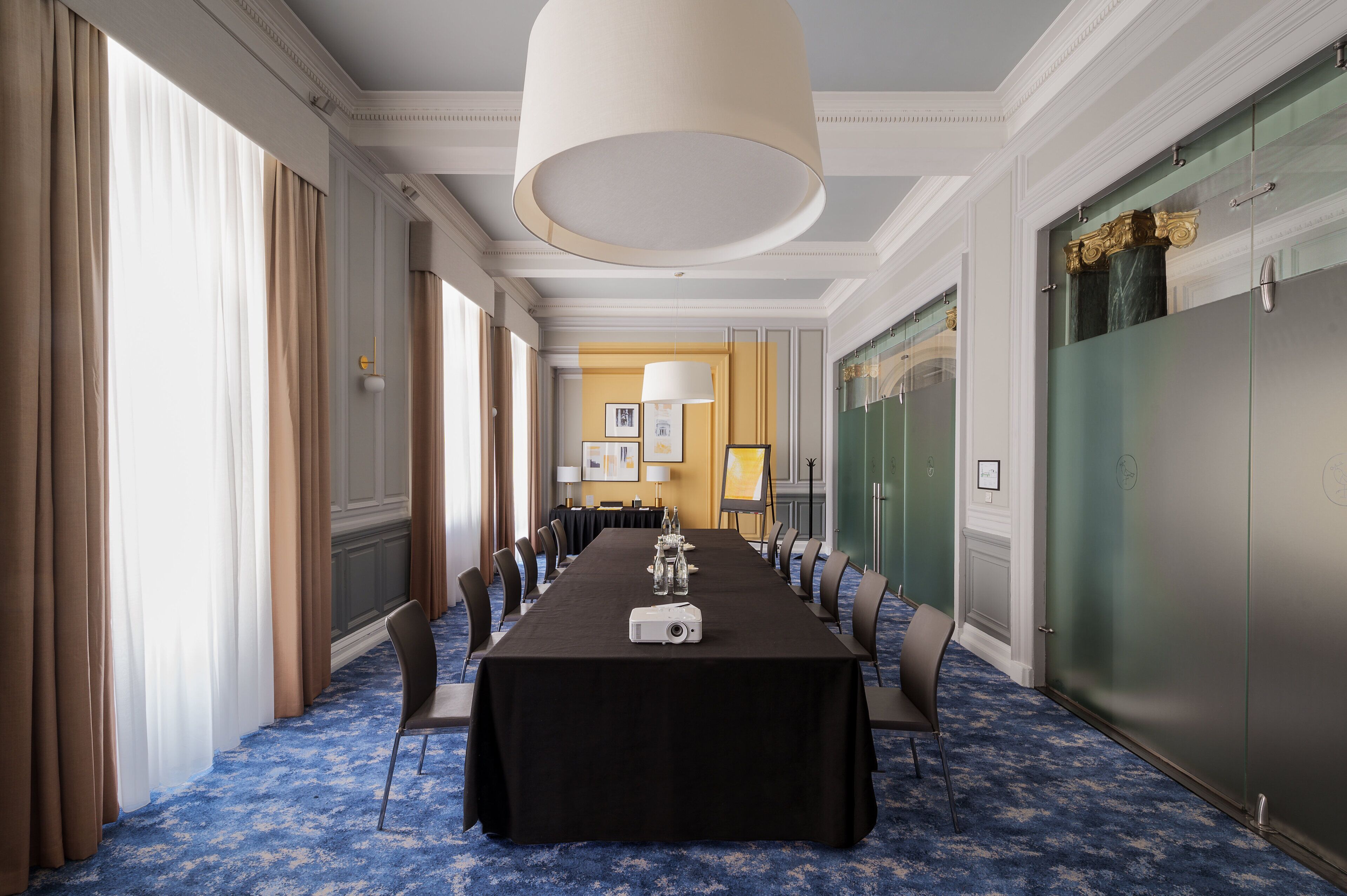 Un salón de conferencias con una larga mesa, sillas, un proyector y una lámpara colgante grande.