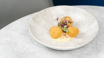 A white ceramic plate with three round, golden-brown items and a creamy sauce, garnished with microgreens, on a marble surface.