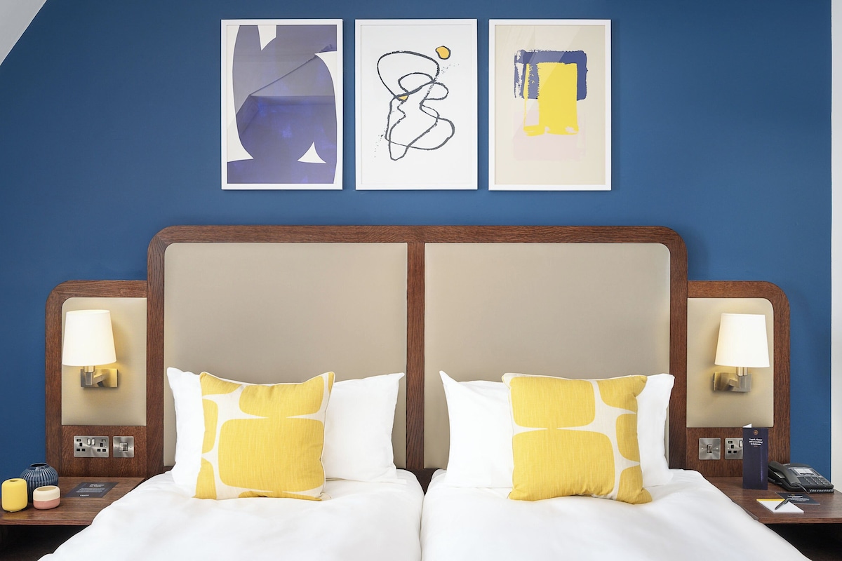 Una habitación de hotel con una cama grande, dos mesitas de noche y tres obras de arte colgadas en la pared.
