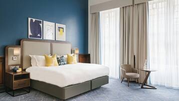 Quarto de hotel com uma cama grande, uma cadeira, uma mesinha e obras de arte na parede.