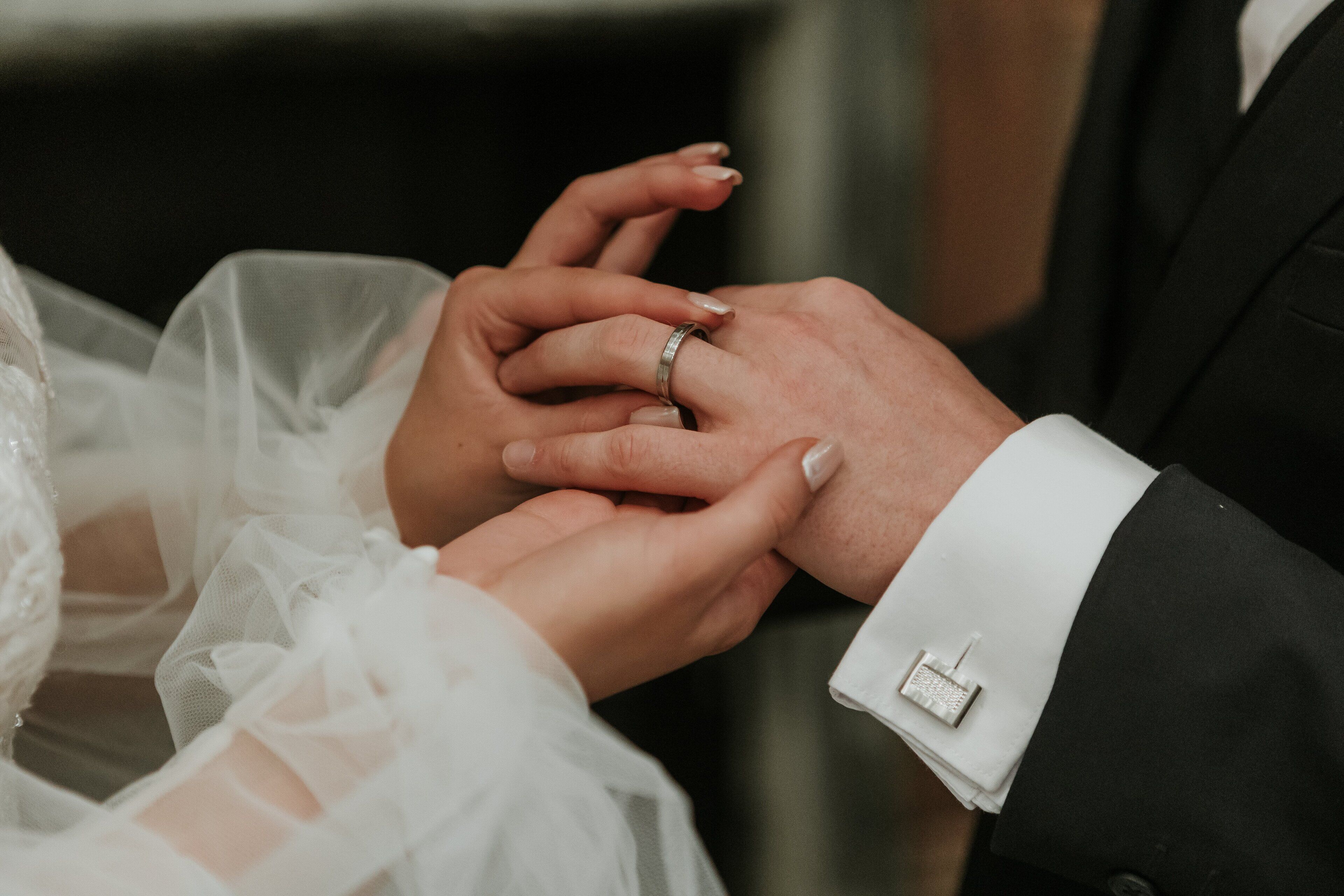 A close-up of hands exchanging rings, one wearing a wedding ring.