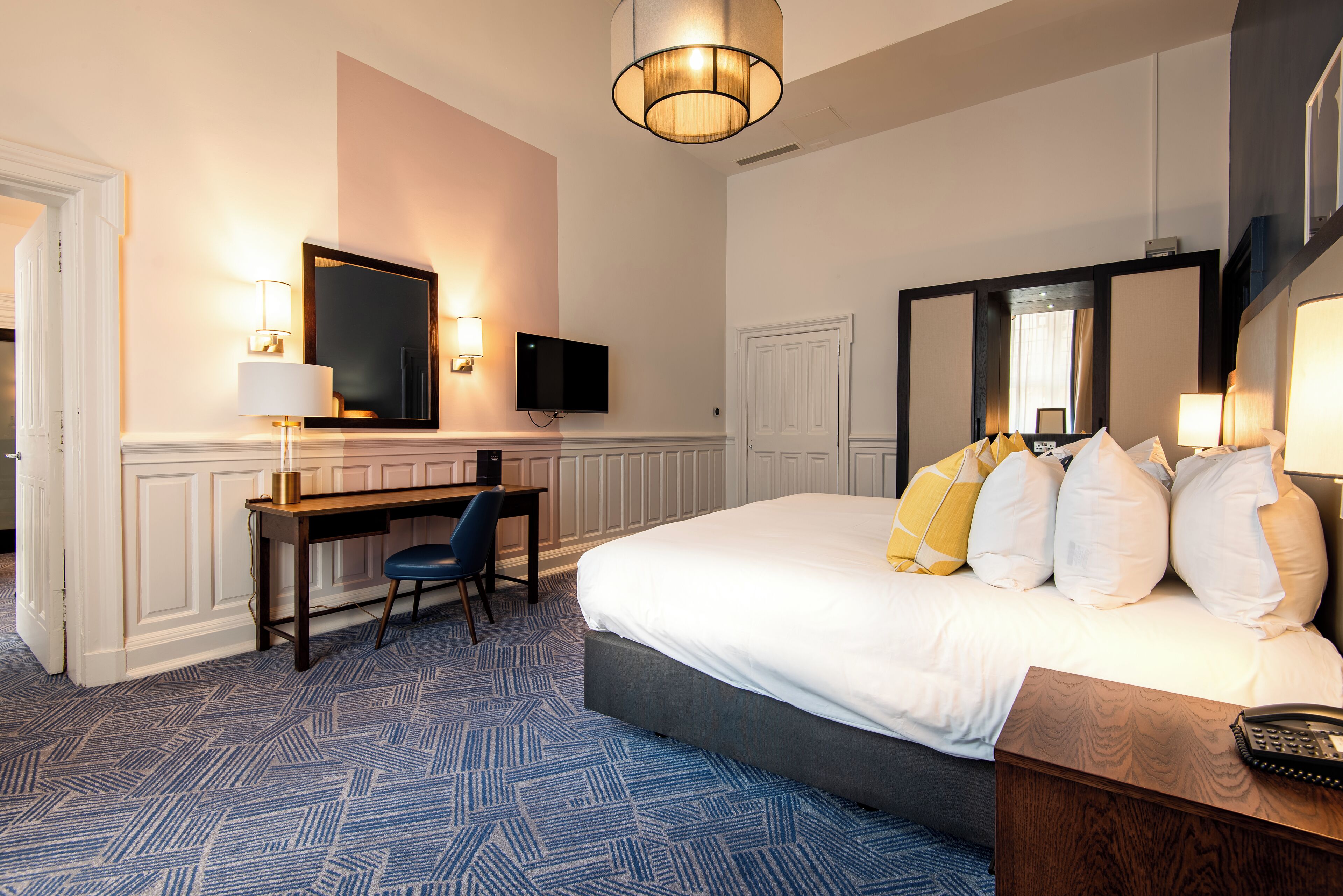 A hotel room with a bed, desk, chair, and a television.