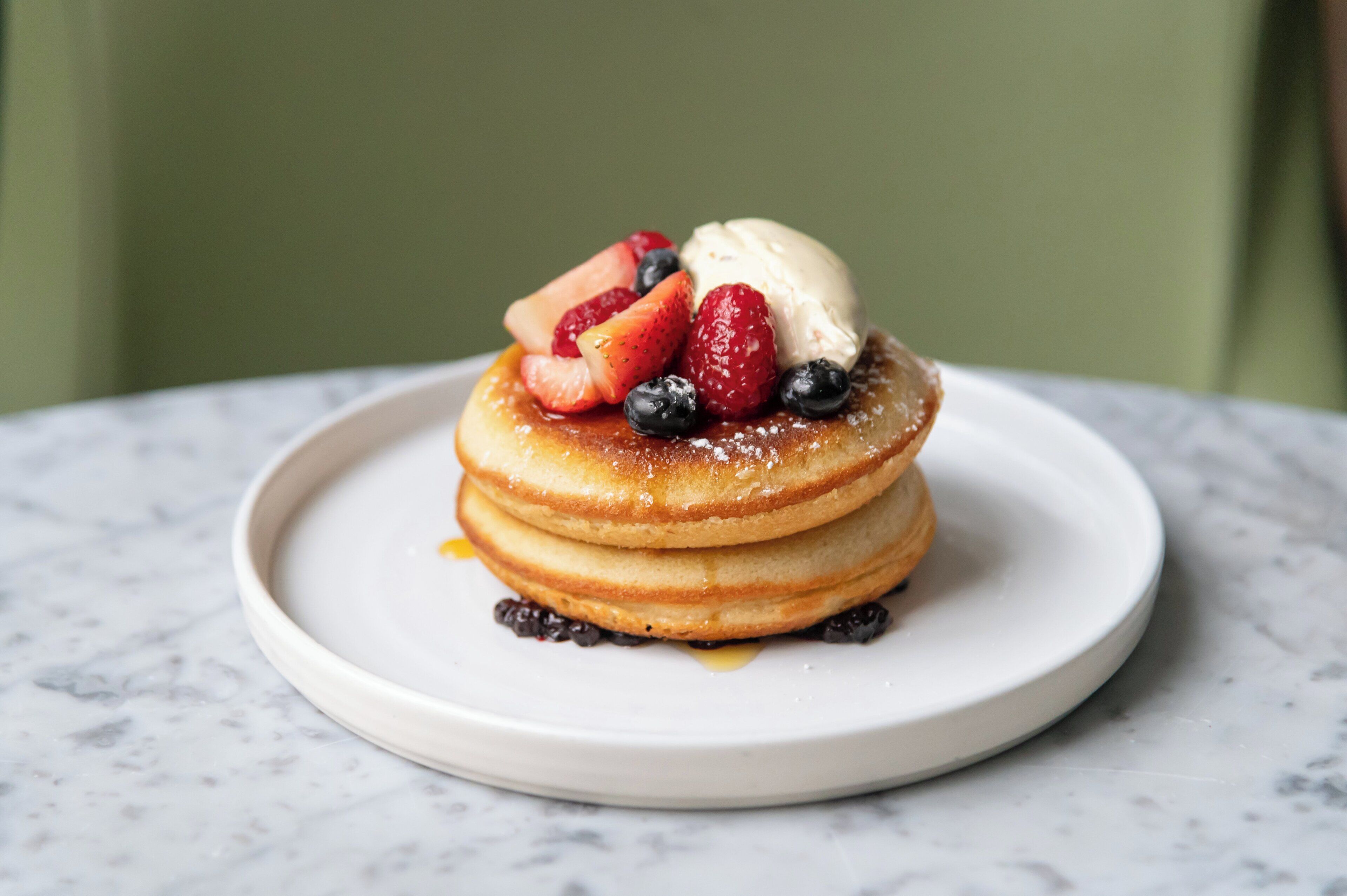 A stack of pancakes with fruit and ice cream on a white plate.