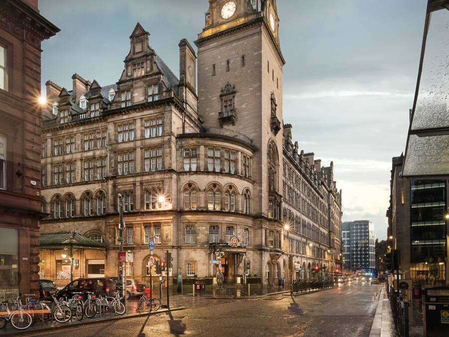 Un edificio storico con una torre dell'orologio, ampie finestre e un ingresso ad angolo.