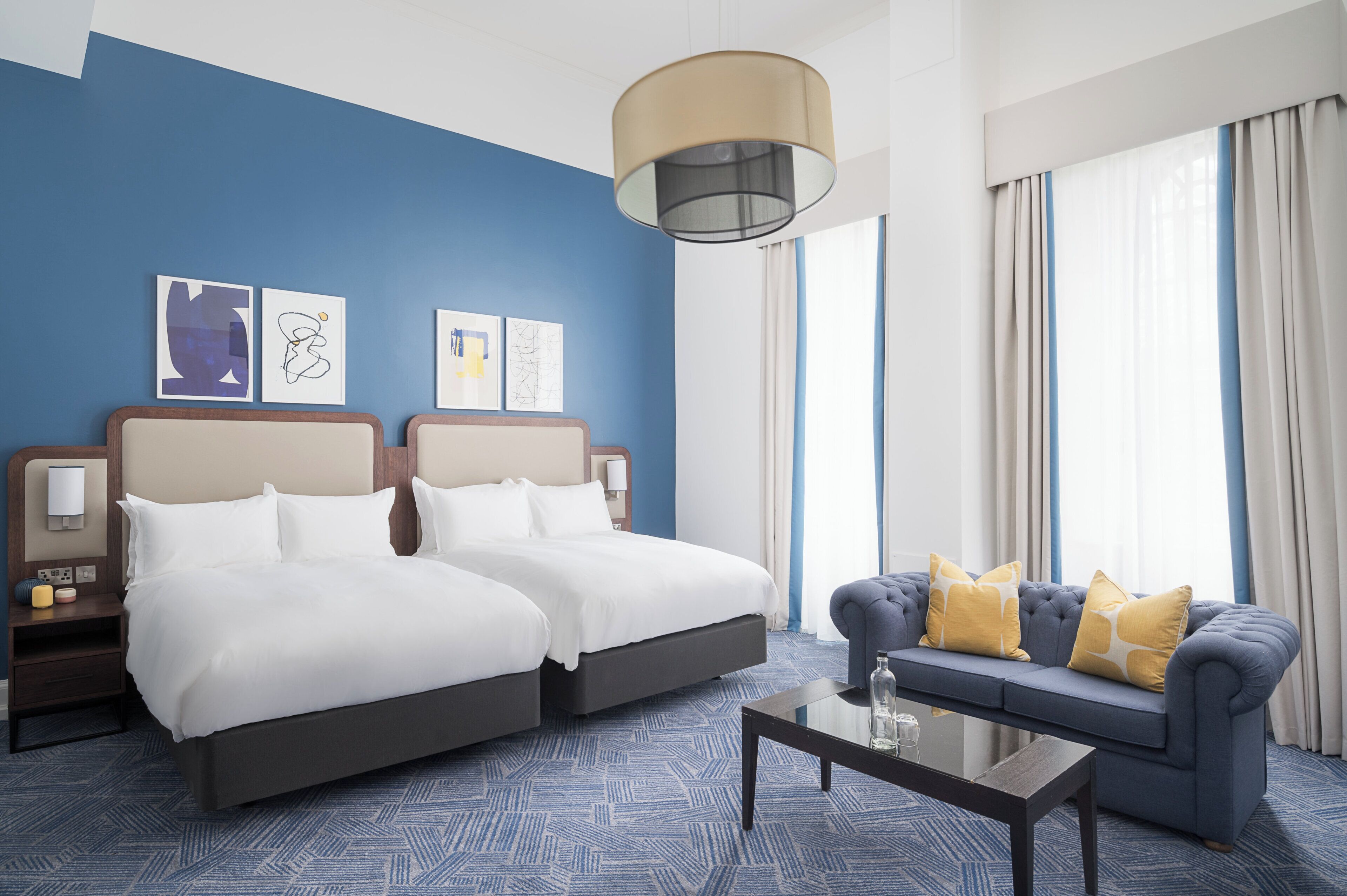 A hotel room with two beds, a sofa, a coffee table, and artwork on the wall.
