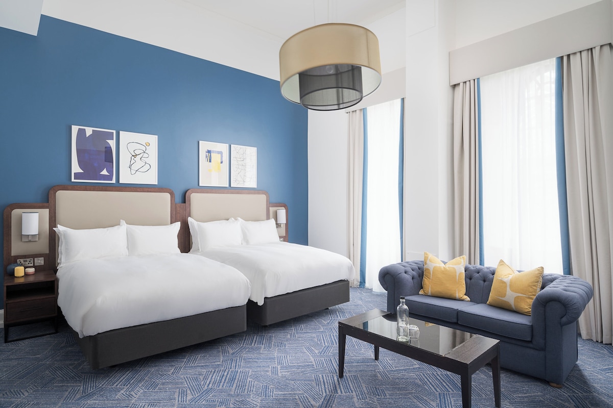 Habitación de hotel con dos camas, un sofá, una mesa de centro y obras de arte en las paredes.