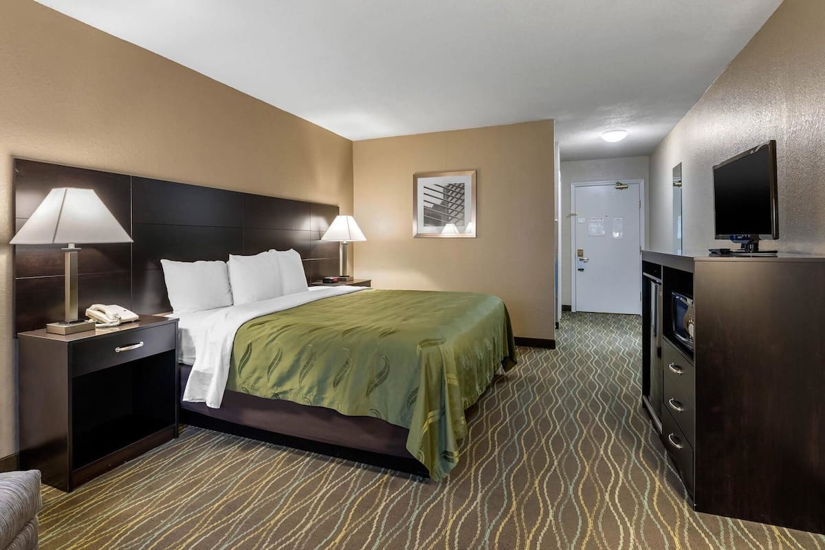 A hotel room with a bed, two bedside lamps, a telephone, a television, a dresser, and a door.