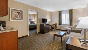 Ein Hotelzimmer mit Küchenzeile, einem Bett, einem Fernseher, einem Schreibtisch, einem Stuhl und einer Couch.
