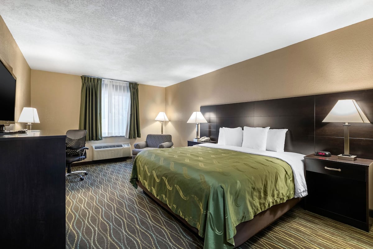 A hotel room with a large bed, two bedside lamps, a desk with a lamp, a chair, a TV, and a window with curtains.