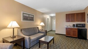 Ein Hotelzimmer mit einer Couch, zwei Lampen, einem kleinen Tisch und einer Küchenzeile mit einer Mikrowelle und einem Kühlschrank.