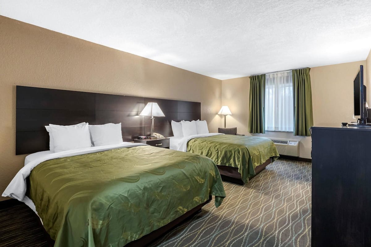 A hotel room with two beds, a desk, a TV, and a window with curtains.