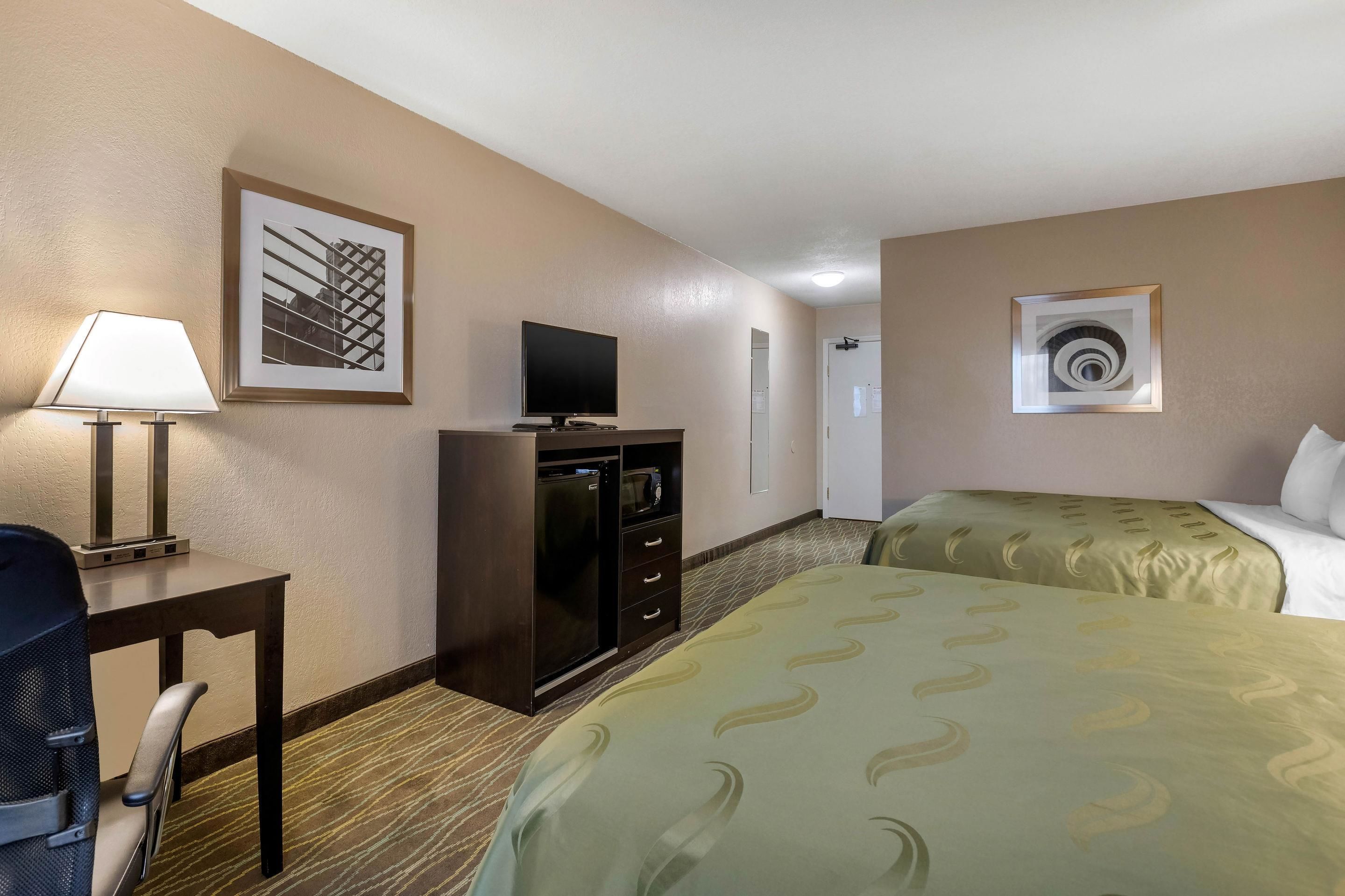 Een hotelkamer met een bureau, een televisie, een bed en een kunstwerk aan de muur.