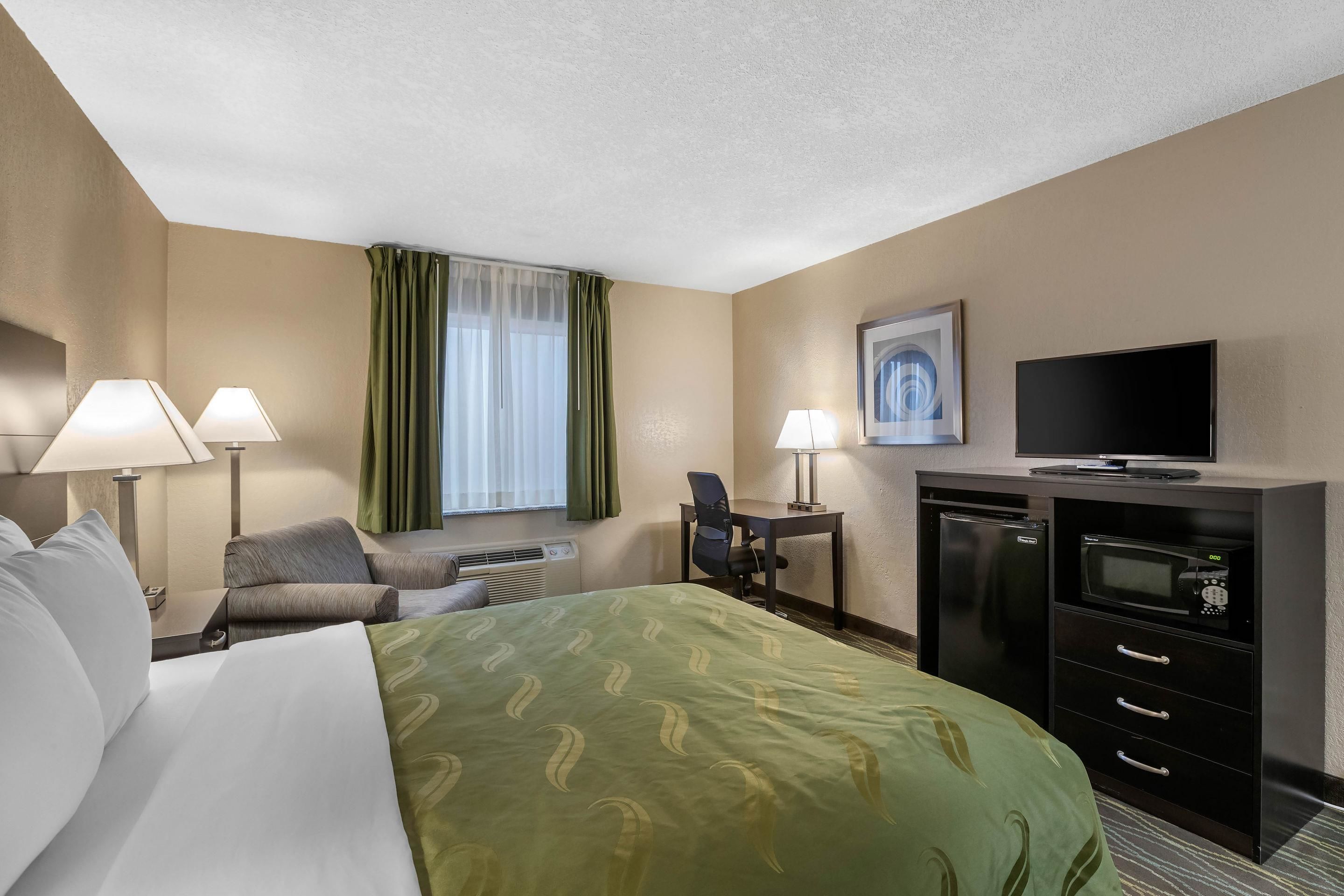 A hotel room with a bed, two chairs, a desk with a computer, a TV, and a microwave.