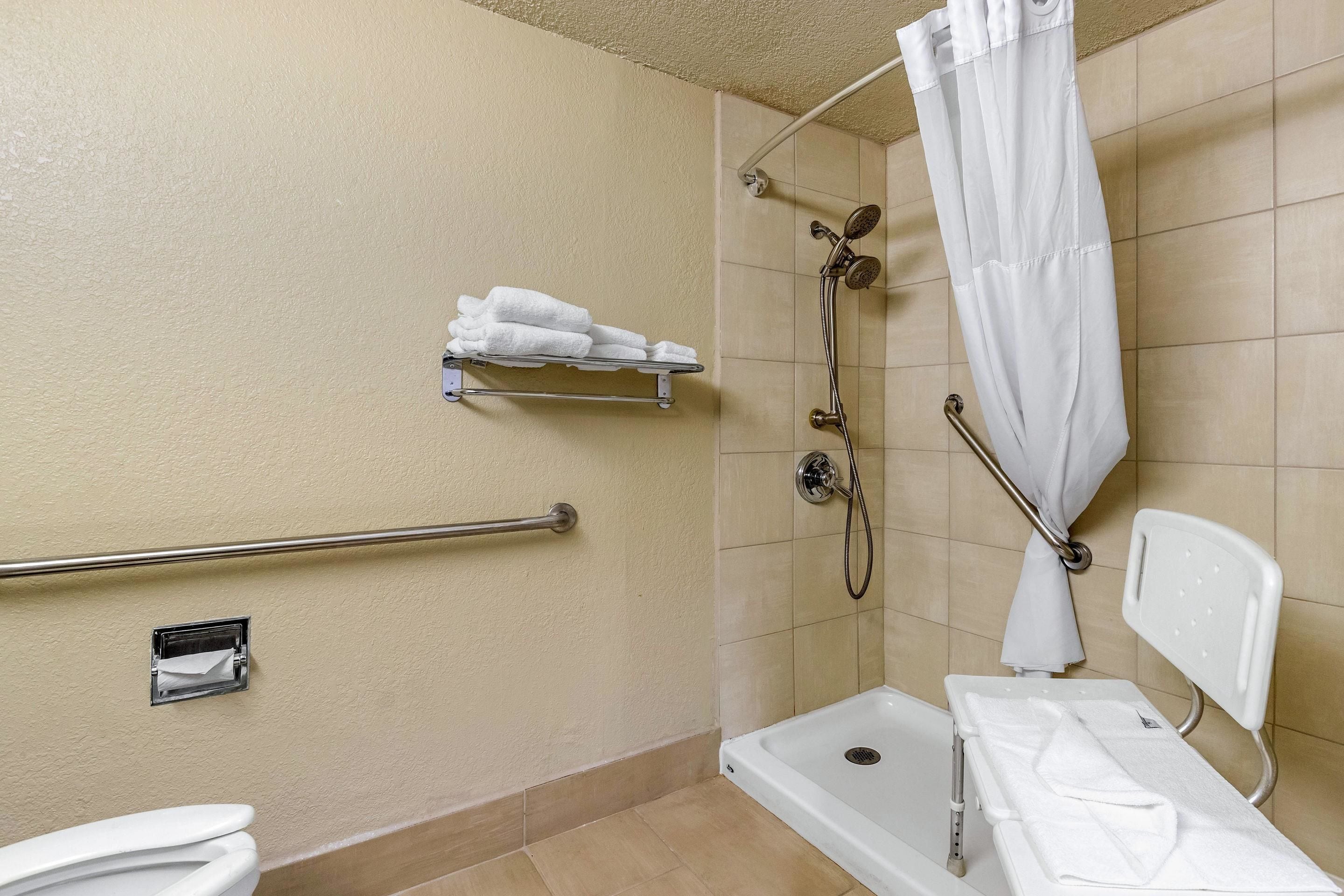 Un baño con ducha, barra de apoyo, inodoro y banco.